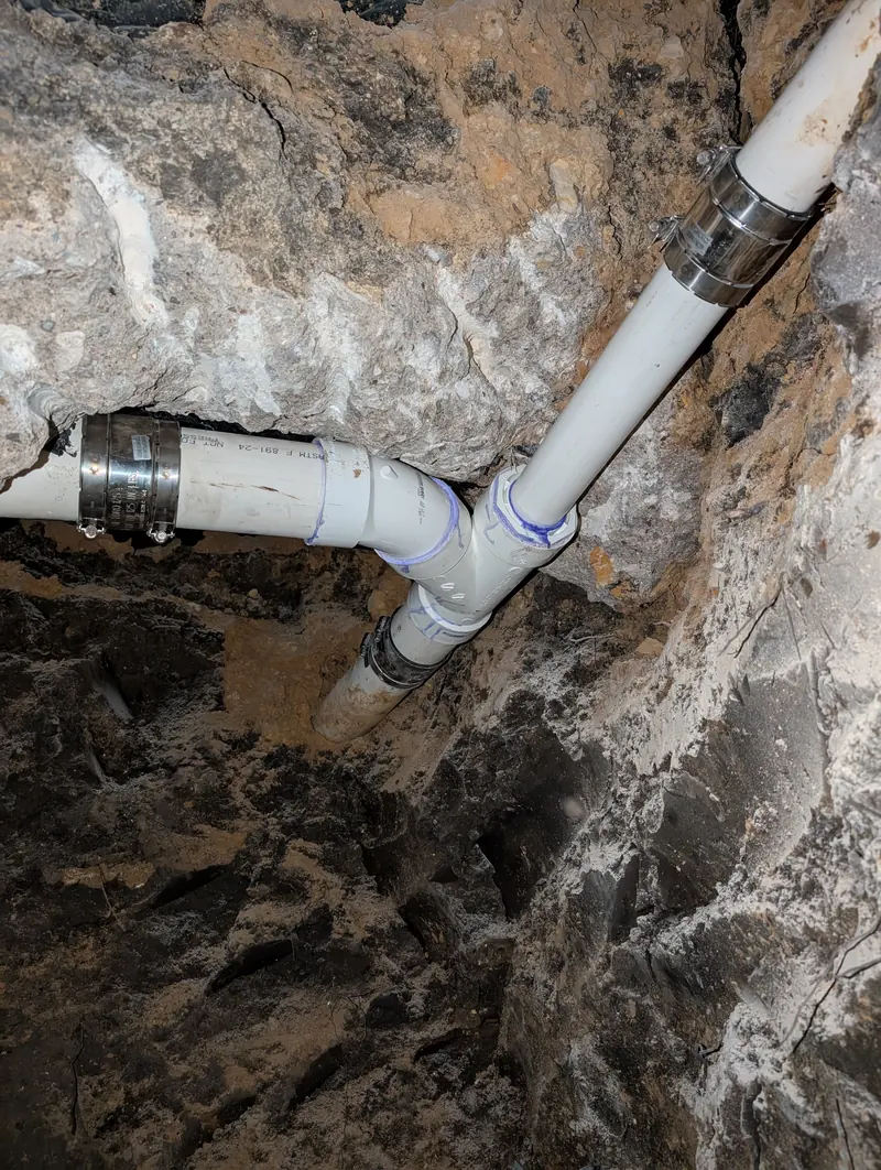A repiped PVC sewer branch joined with shielded couplings, tunnelled through rock beneath a house slab.
