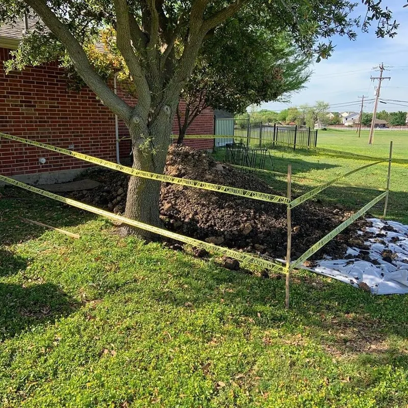 A sewer excavation in a back yard beside a brick house, roped off with caution tape, the excavated soil piled on plastic sheeting to protect the lawn.